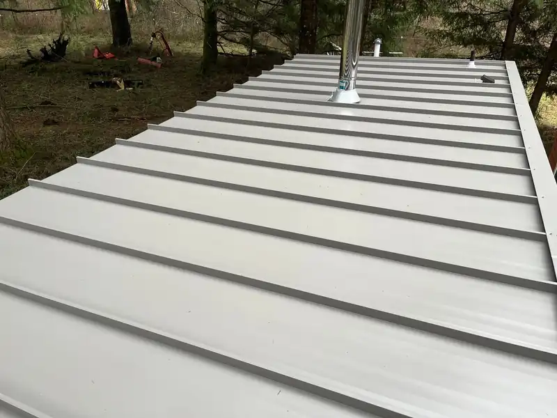Silver standing-seam panel run with a pipe flashing, open field beyond