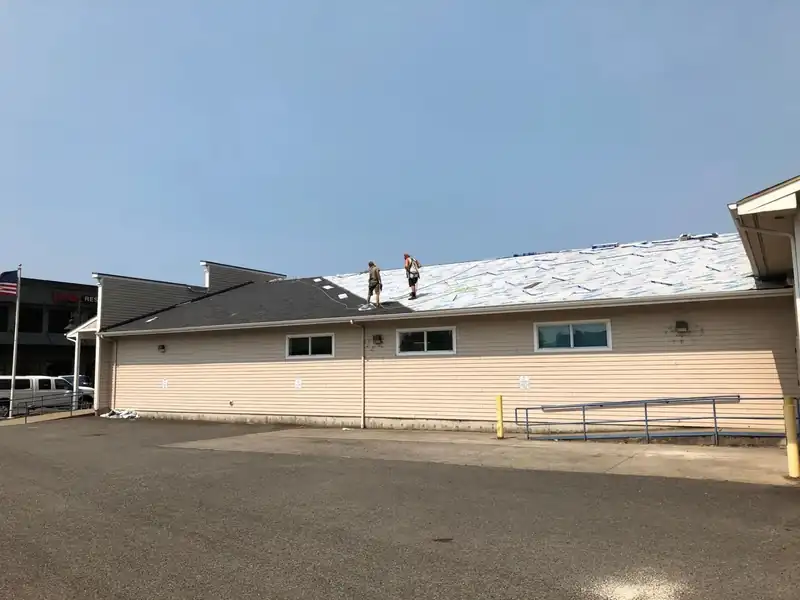 Single-storey commercial building with white underlayment and a crew on the roof